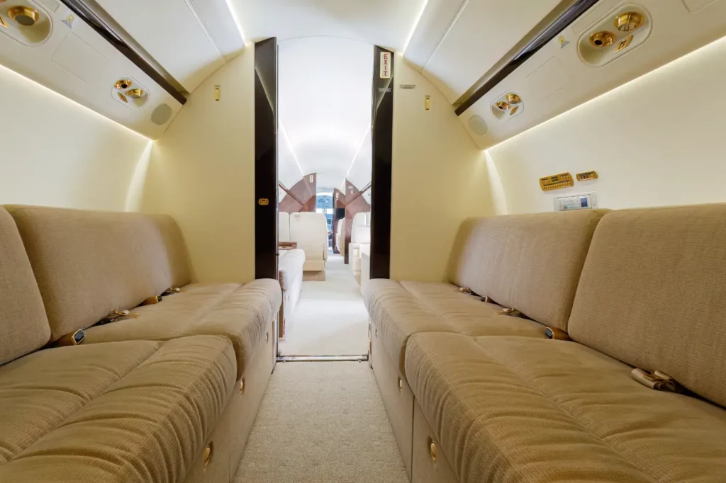 Interior view of the Gulfstream G550's aft cabin, displaying plush beige divans and luxurious seating arrangements with ambient lighting.