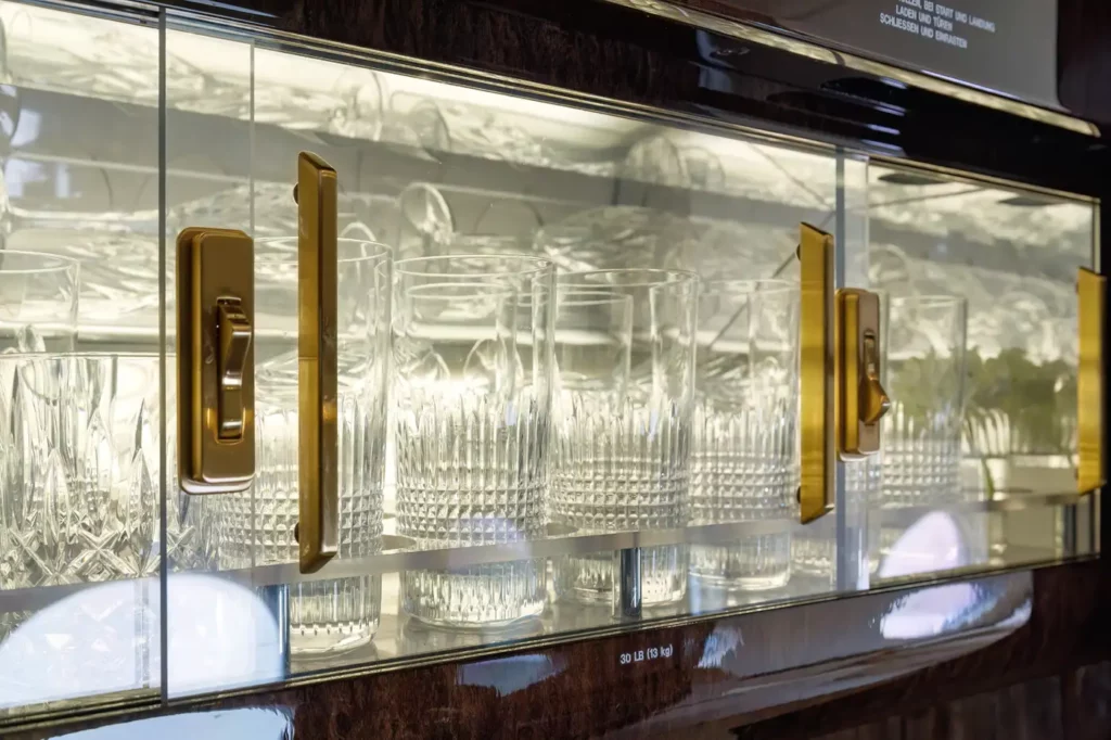 Detail shot of a cabinet inside the Gulfstream G550, displaying neatly arranged crystal glassware behind gold-handled glass doors.