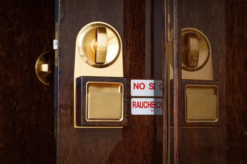 Close-up of a cabin door on the Gulfstream G550, highlighting the luxurious wooden finish and gold-plated hardware, alongside a "No Smoking" sign.