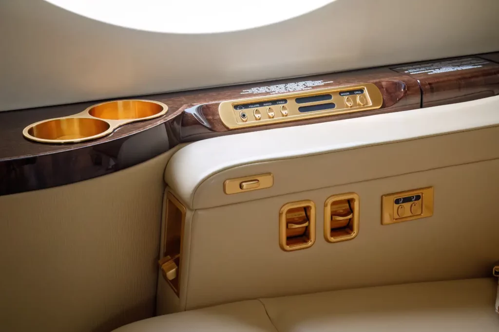 Interior detail of the Gulfstream G550, showing a control panel and cup holders with gold accents near a passenger seat.