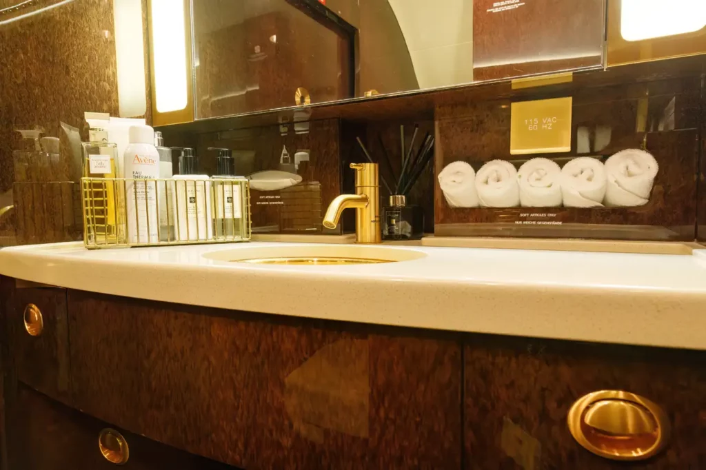 Executive lavatory in the Gulfstream G550, featuring a well-equipped vanity with a gold faucet, toiletries, and rolled towels on display.