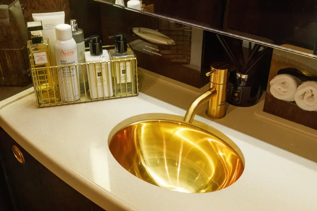 Close-up view of the executive lavatory in the Gulfstream G550, featuring a gold sink and faucet, with various luxury toiletries displayed in a gold rack.