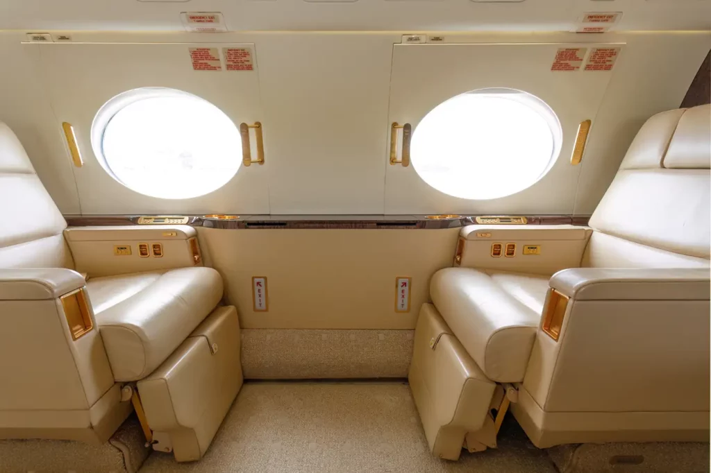 Interior view of the executive club seating area in the Gulfstream G550, showing two plush leather seats and large oval windows providing natural light.