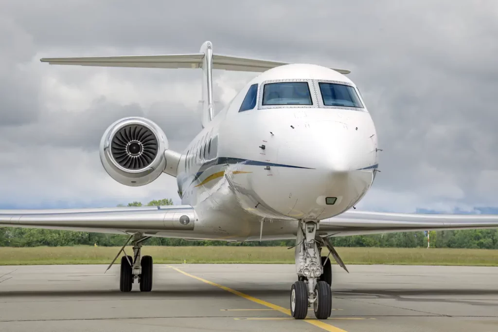 Front view of the Gulfstream G550 on the tarmac, highlighting the aircraft's sleek nose and powerful engine against a cloudy sky.