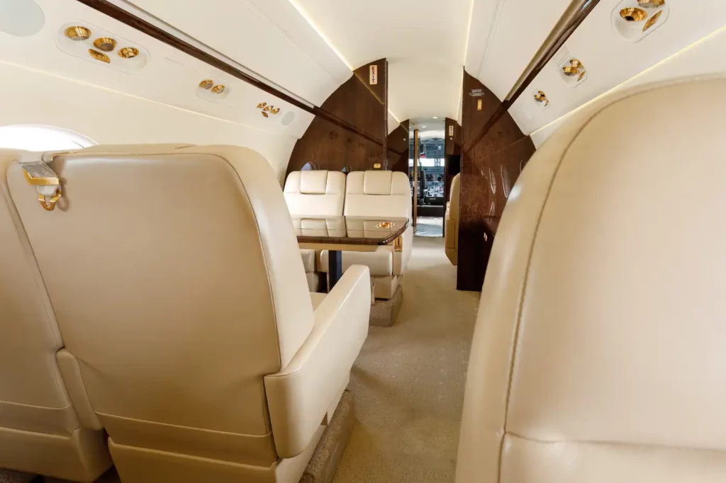 Forward view of the executive club seating area in the Gulfstream G550, displaying comfortable leather seats and a central table, leading towards the cockpit.