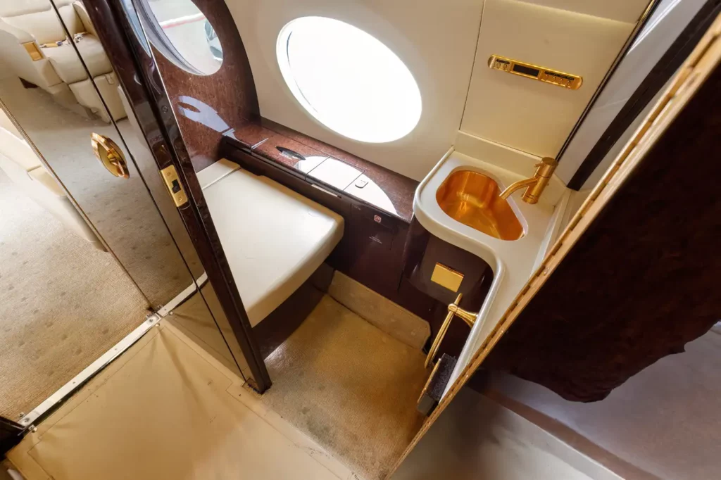 Lavatory in the Gulfstream G550, featuring a gold sink and faucet, plush carpet, and a window providing natural light.