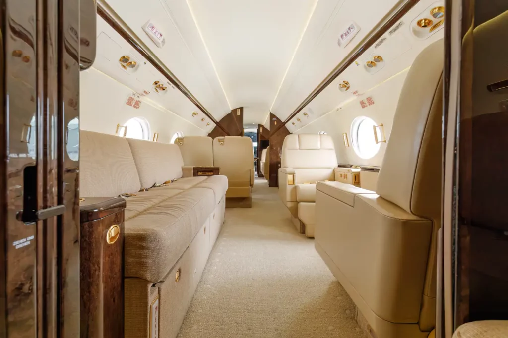 Interior shot looking from the mid-cabin towards the front of the Gulfstream G550, showing the arrangement of seats and tables with the cockpit visible in the background.