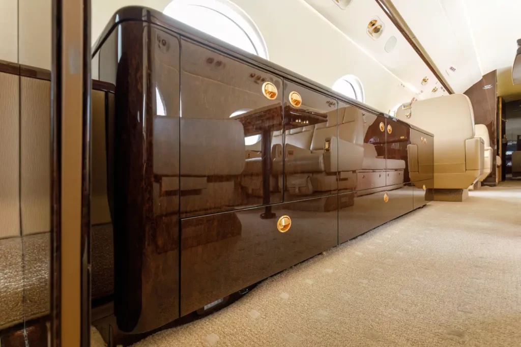 Interior view of the Gulfstream G550, highlighting a glossy wood side console with gold hardware, reflecting the luxurious seating and table setup.