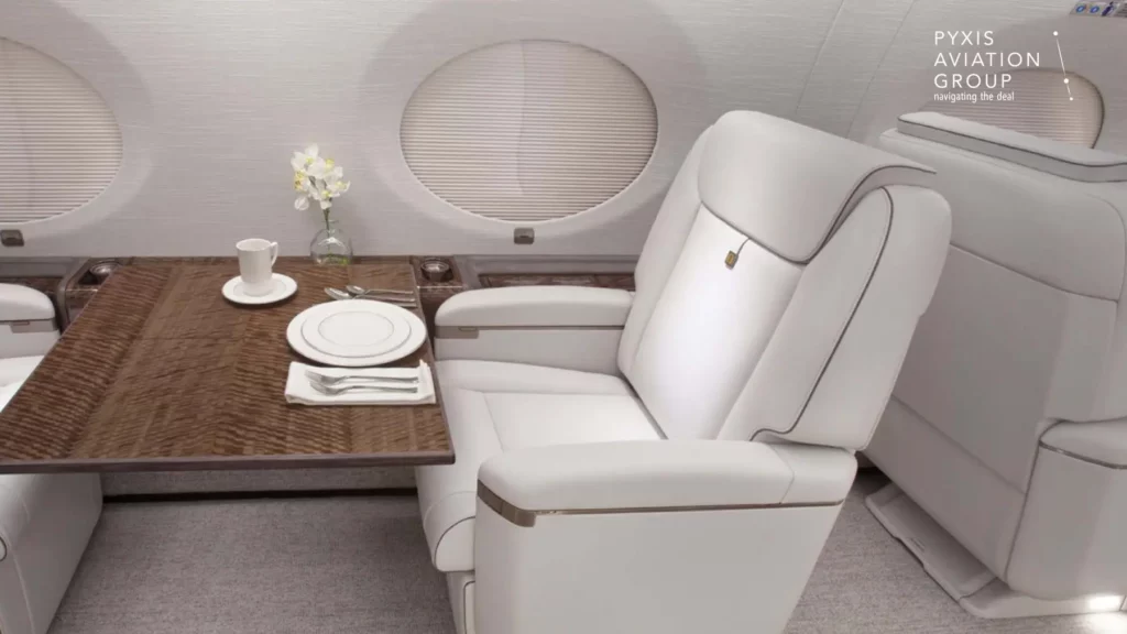 A dining setup within the Gulfstream G650 jet's cabin, showcasing a large wooden table set with fine china, a cup, and silverware. The seating includes plush white leather chairs, with a small vase of flowers adding a touch of elegance to the luxurious in-flight dining experience.