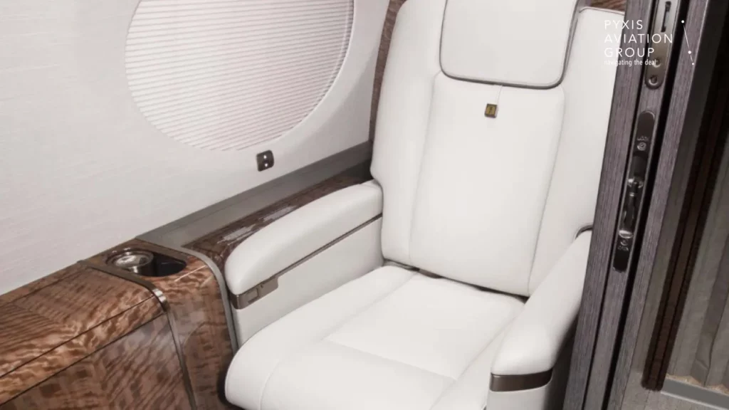 A luxurious single-seat detail within the Gulfstream G650 jet, featuring a white leather seat with armrests, set beside a polished wood side console. The area exudes sophistication with its minimalist design and high-quality materials, emphasizing comfort and elegance.