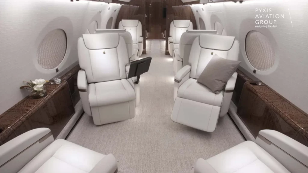 Forward-mid cabin of a Gulfstream G650 jet, showcasing four large, white leather reclining seats arranged in a club seating configuration. The cabin is elegantly designed with polished wood accents and soft lighting, providing a spacious and comfortable atmosphere.