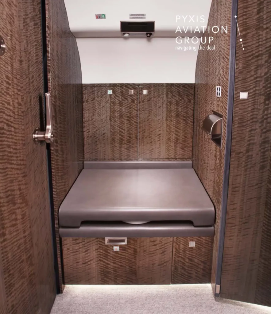 Lavatory area in a Gulfstream G650 jet, featuring a sleek and modern design with rich wood paneling and a fold-down seat. The compact space is designed with functionality in mind, providing a luxurious yet practical environment for passengers.