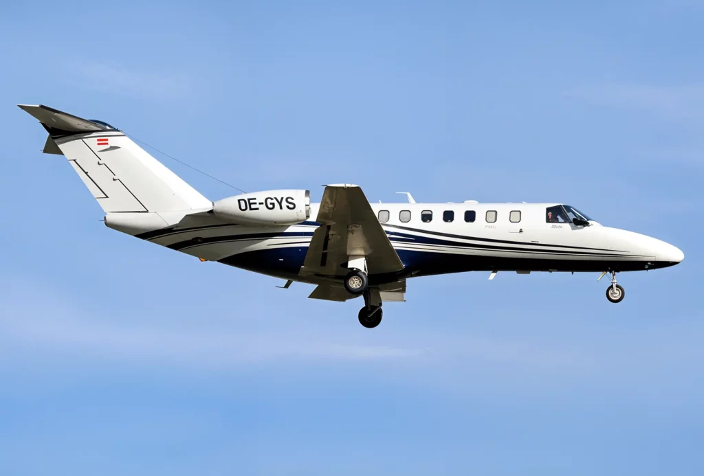 Side view of a Cessna Citation CJ3 in flight with registration number OE-GYS, highlighting its sleek design and white exterior with blue accents against a clear blue sky.