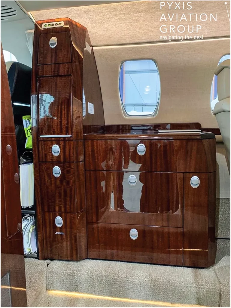 Galley area of a Cessna Citation CJ3 with polished wood cabinetry, storage compartments, and a countertop, illustrating the aircraft's elegant and functional design.