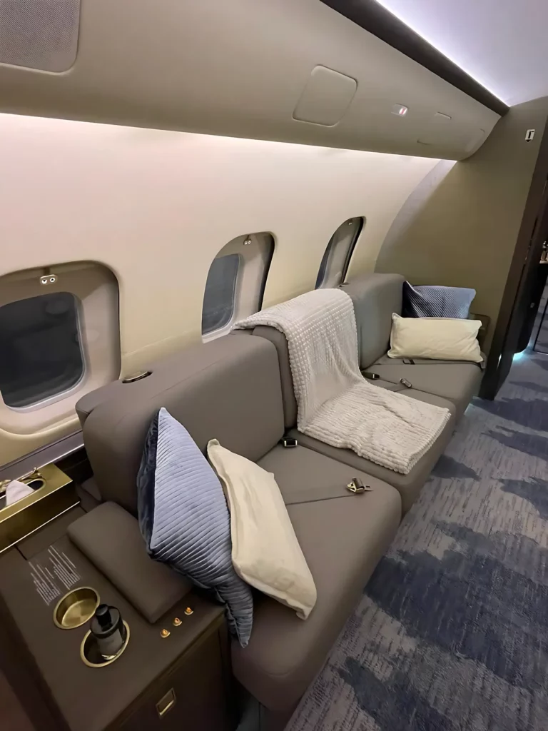 Cozy divan seating area in the Bombardier Global 5000 jet, adorned with plush pillows and blankets.