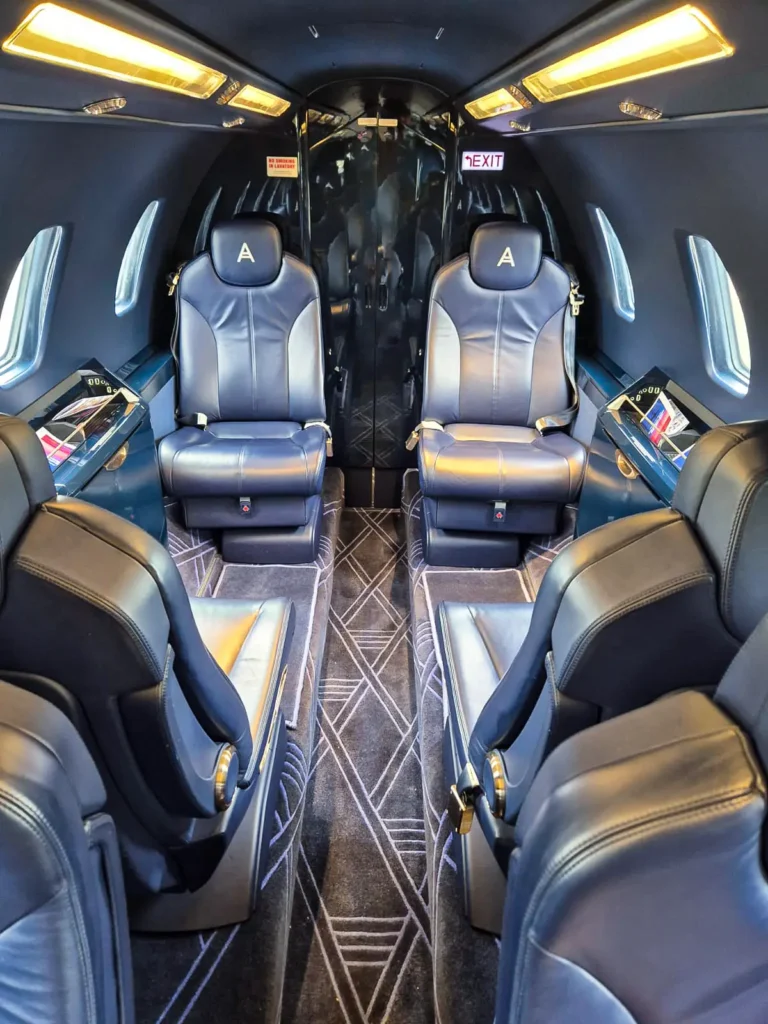 The rear section of the Cessna Citation Sovereign+ private jet cabin featuring four plush leather seats in a face-to-face configuration. The seats have the "A" logo on their headrests, and the space is well-lit, offering a spacious and refined atmosphere for passengers.