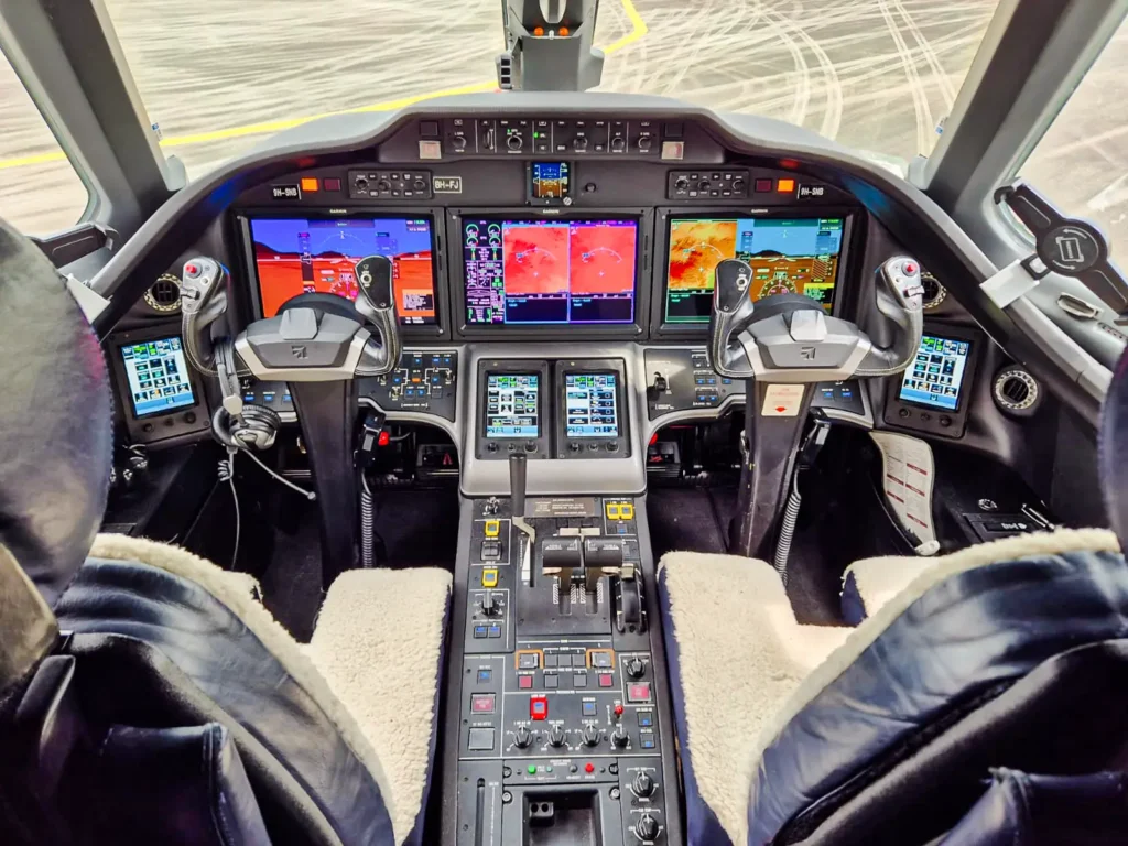 The modern cockpit of a Cessna Citation Sovereign+ featuring dual yokes and multiple digital displays, showing navigation, communication, and aircraft performance data. The center console is filled with control buttons, levers, and screens, all illuminated by the bright display screens. Two pilot seats are visible, both lined with cushioned backrests.