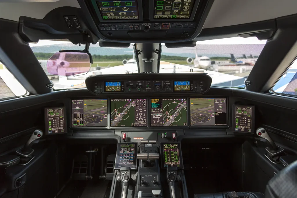 The cockpit of a Gulfstream G600, featuring the Symmetry Flight Deck. The cockpit displays a range of high-tech touchscreens and avionics controls, including several primary flight displays, engine data, and navigation information. The clean, advanced interface with side-stick controls highlights the modern design aimed at enhancing pilot efficiency and situational awareness. Aircraft can be seen parked outside through the cockpit window. By Matti Blume - Own work, CC BY-SA 4.0, Link