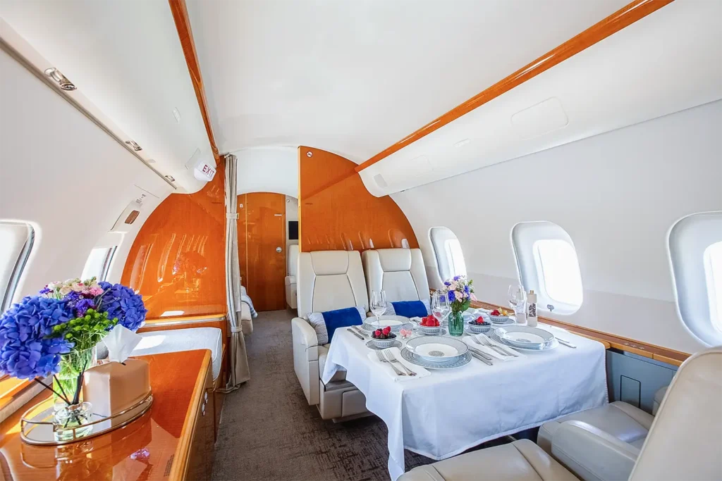 Elegant dining setup inside a Bombardier Global 5000 private jet cabin with cream leather seats, fresh flowers, and fine tableware