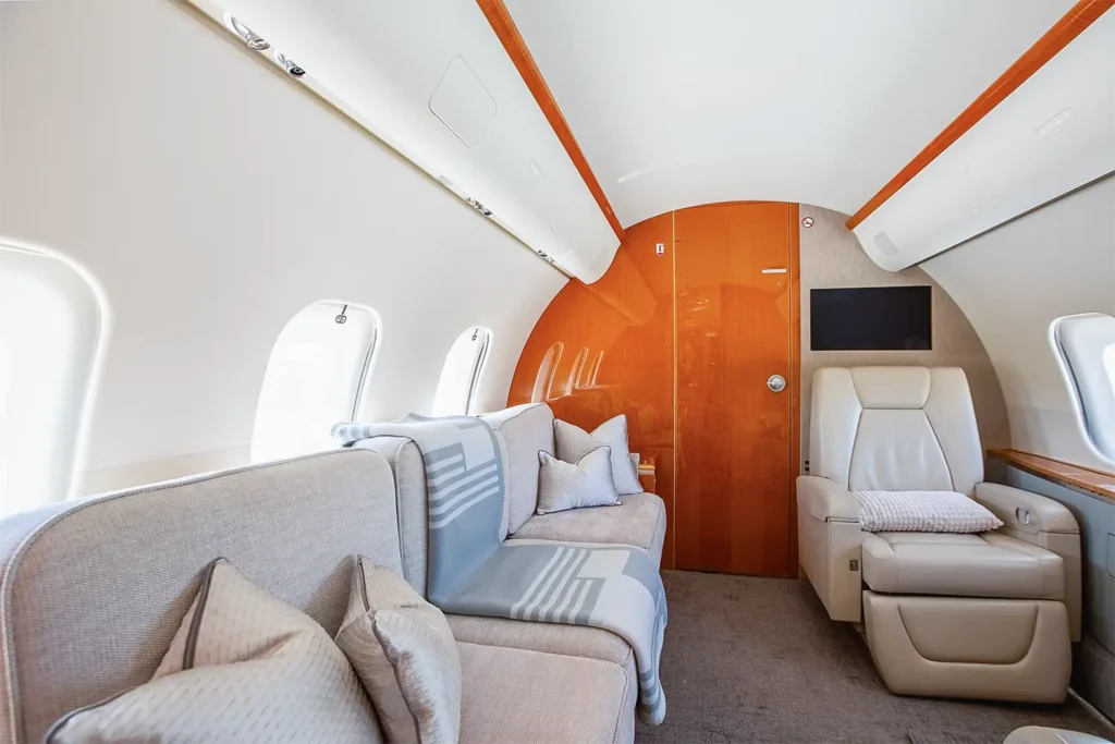 Bombardier Global 5000 private jet interior with luxury seating, a comfortable sofa, and pillows, creating a cozy atmosphere for passengers