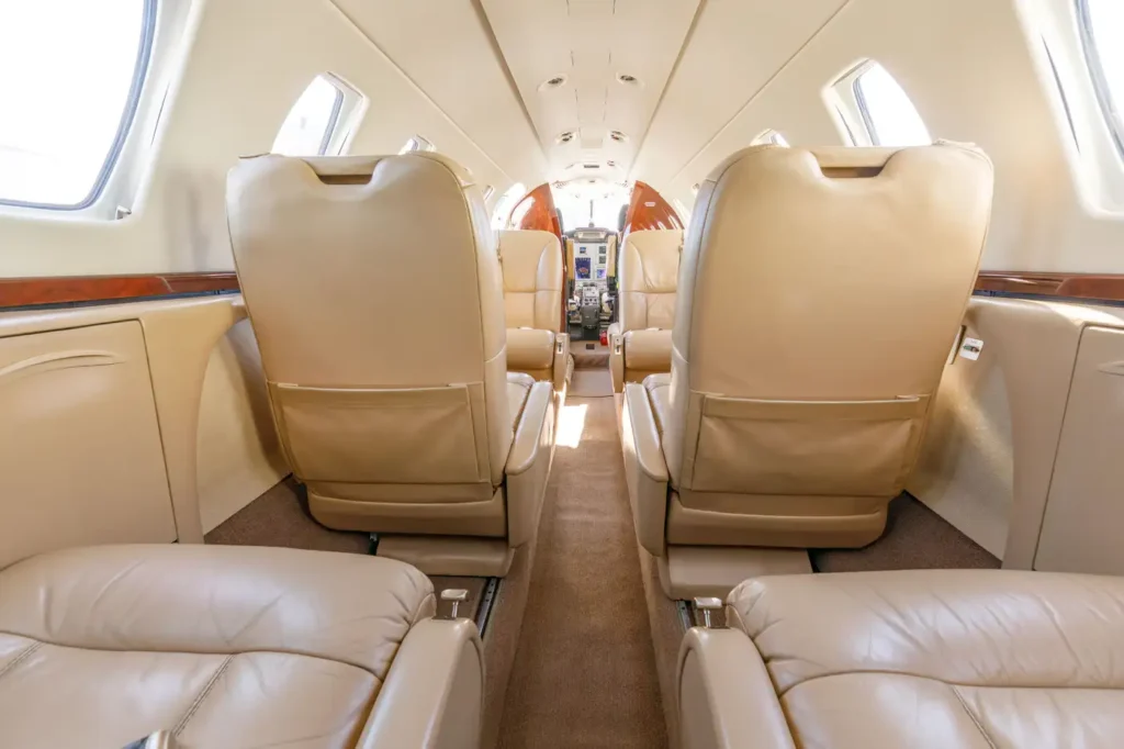 Rear view of the Cessna Citation CJ3 private jet cabin featuring rows of beige leather seats and windows