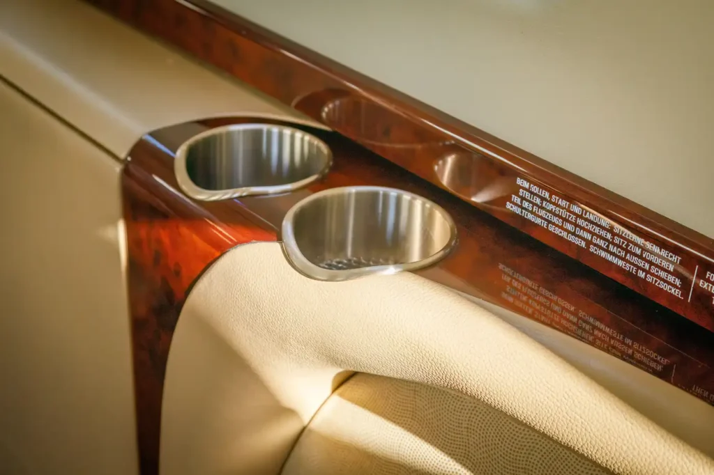 Stainless steel cup holders and wood finish armrest in the cabin of a Cessna Citation CJ3 private jet