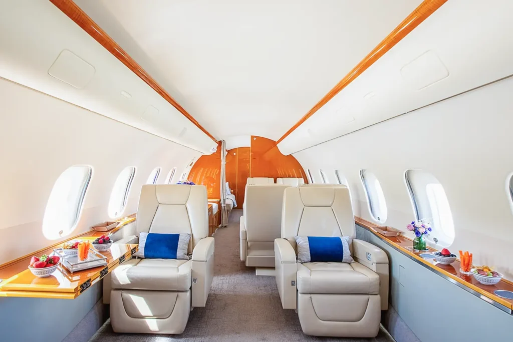 Luxurious Bombardier Global 5000 private jet interior with cream leather reclining seats, wood accents, and fruit platters on the side table