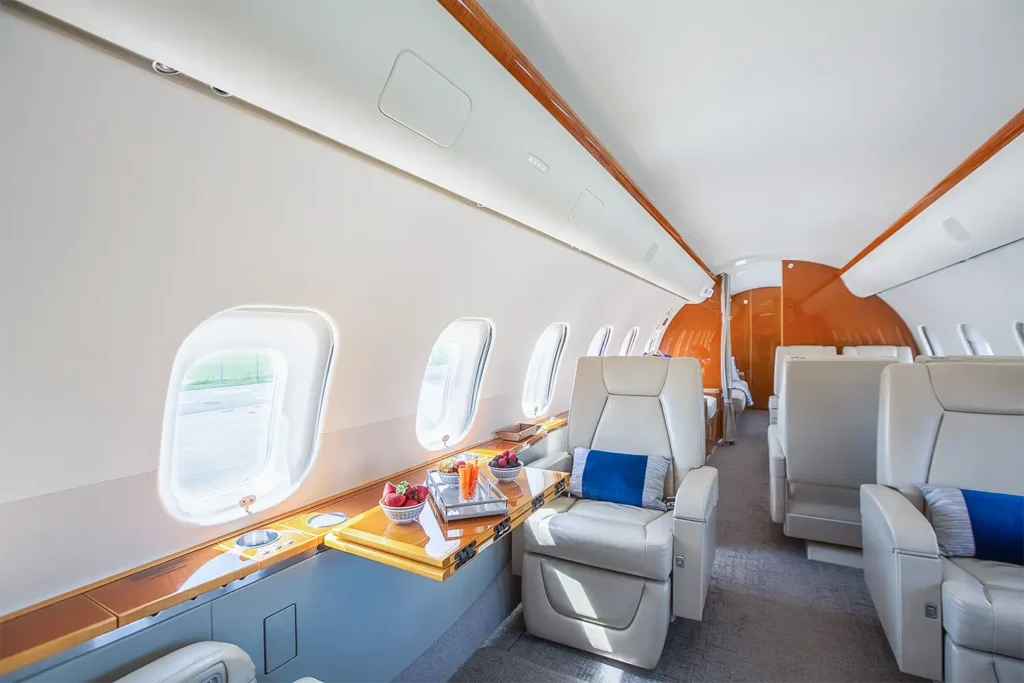 Spacious seating arrangement in a Bombardier Global 5000 private jet cabin featuring cream leather seats and natural light streaming through large windows