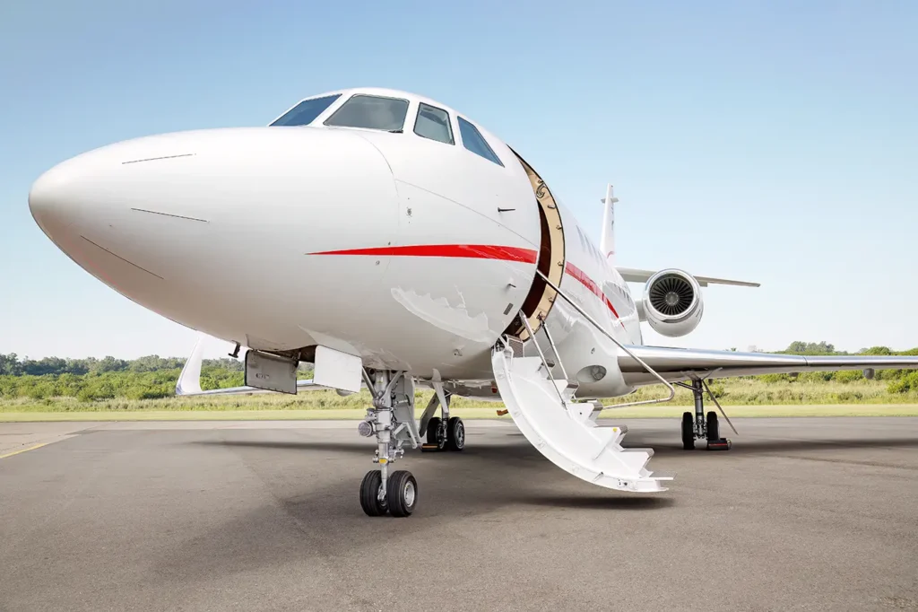 Close-up view of the Dassault Falcon 2000's nose, showcasing its sleek white fuselage with a red stripe and a retractable entry staircase under a clear blue sky.