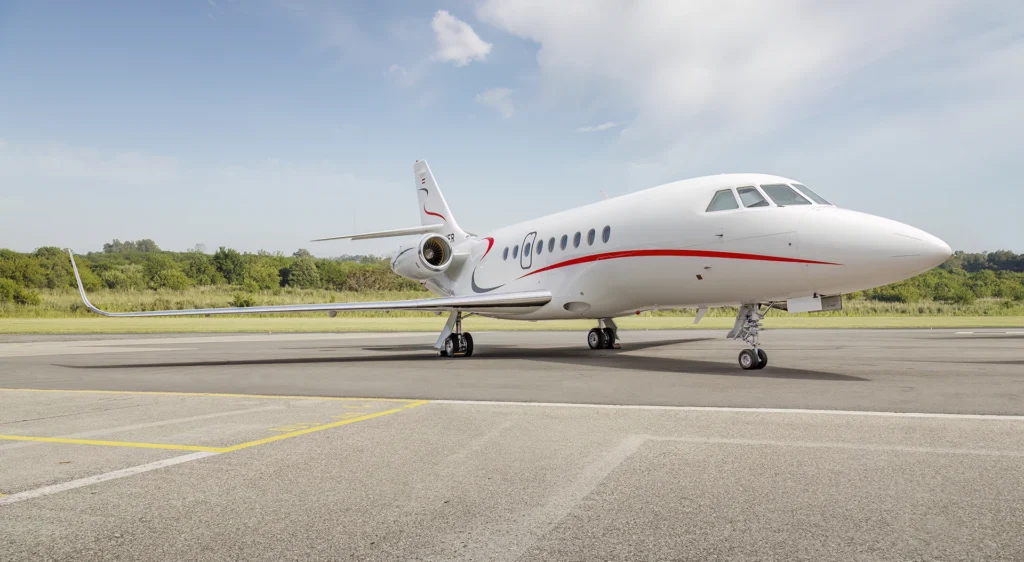 Full side view of the Dassault Falcon 2000 on the tarmac, with its elegant white body, extended wings, and signature red accent stripe