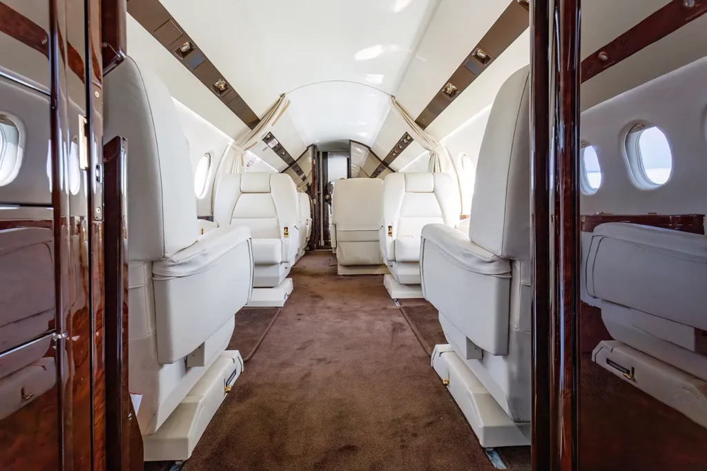 Interior of the Dassault Falcon 2000 private jet cabin, featuring plush cream-colored leather seats and spacious aisles designed for comfort and luxury.