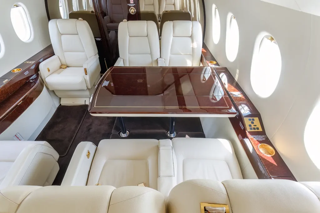 Seating area of the Dassault Falcon 2000 private jet with a glossy wooden table surrounded by cream leather seats, designed for dining or business meetings mid-flight.