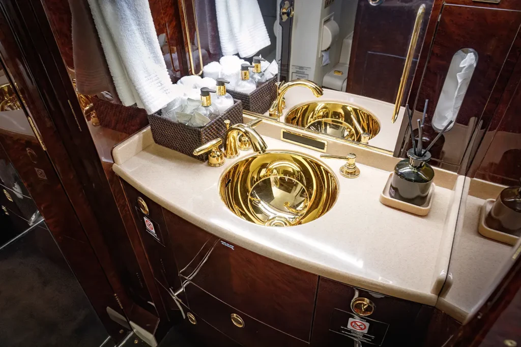 Luxurious bathroom onboard a Dassault Falcon 2000 private jet, featuring gold-plated fixtures, a marble countertop, and premium toiletries for a sophisticated inflight experience.